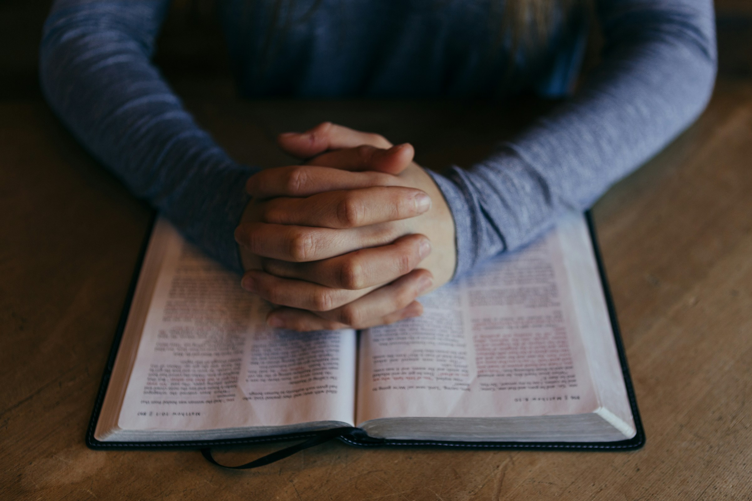 Open Bible and folded hands in prayer